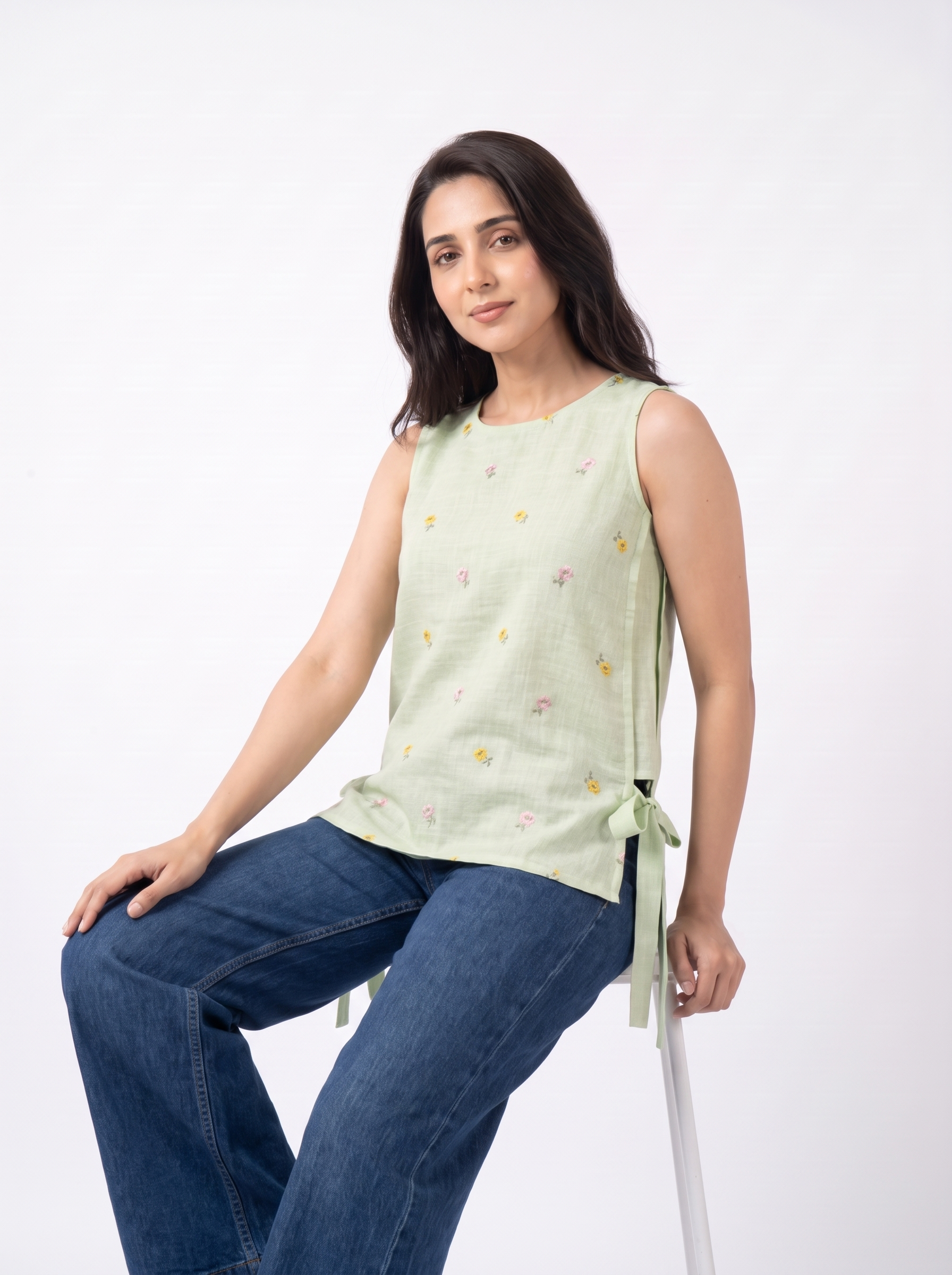 Add a soft feminine touch to your wardrobe with this sage green sleeveless top, featuring delicate multicolor floral embroidery scattered across the front, a clean round neckline, and stylish side tie-up detailing.