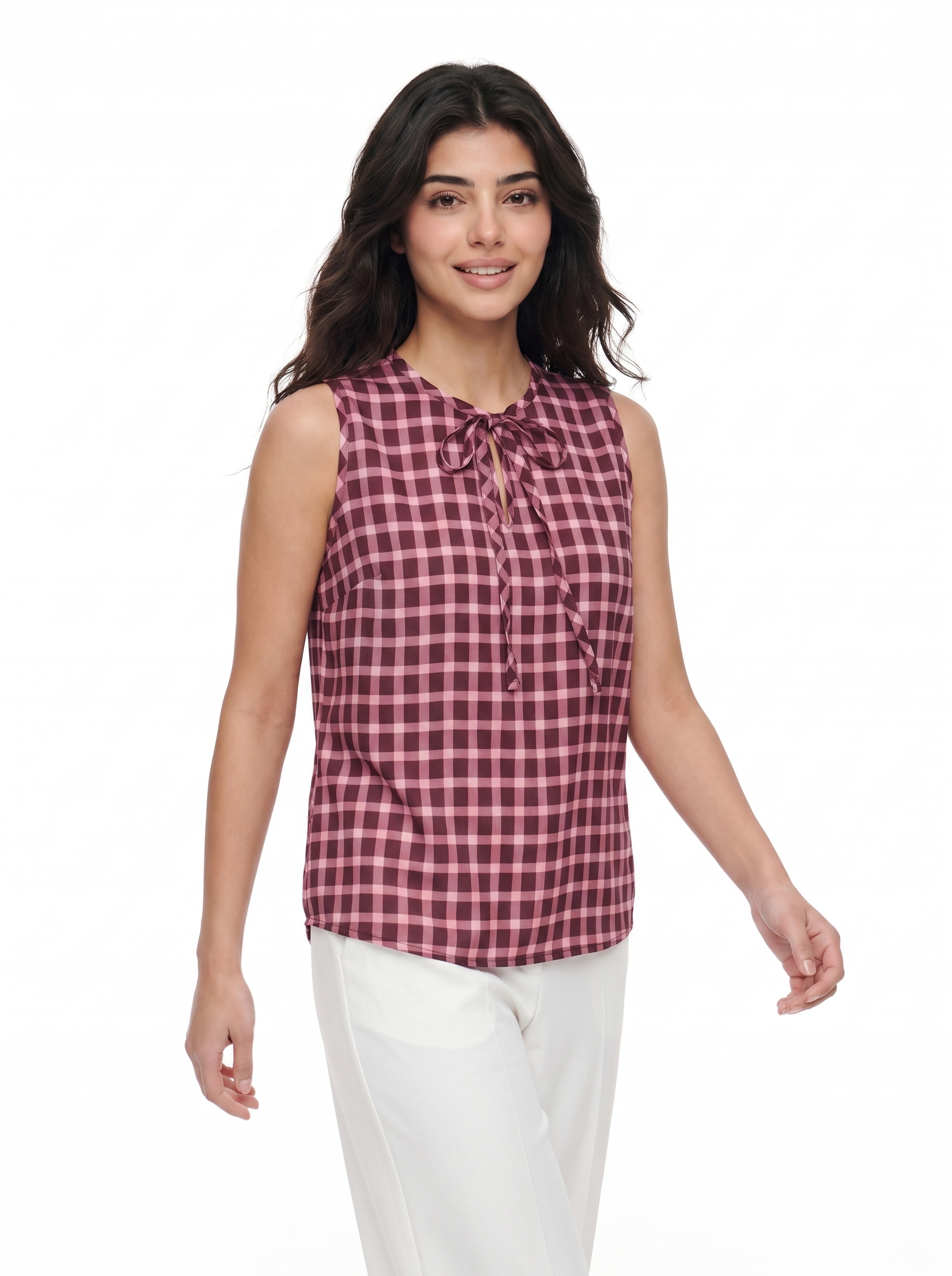 A woman modeling a sleeveless red and black gingham tie-neck blouse with white pants, shot against a solid white background.