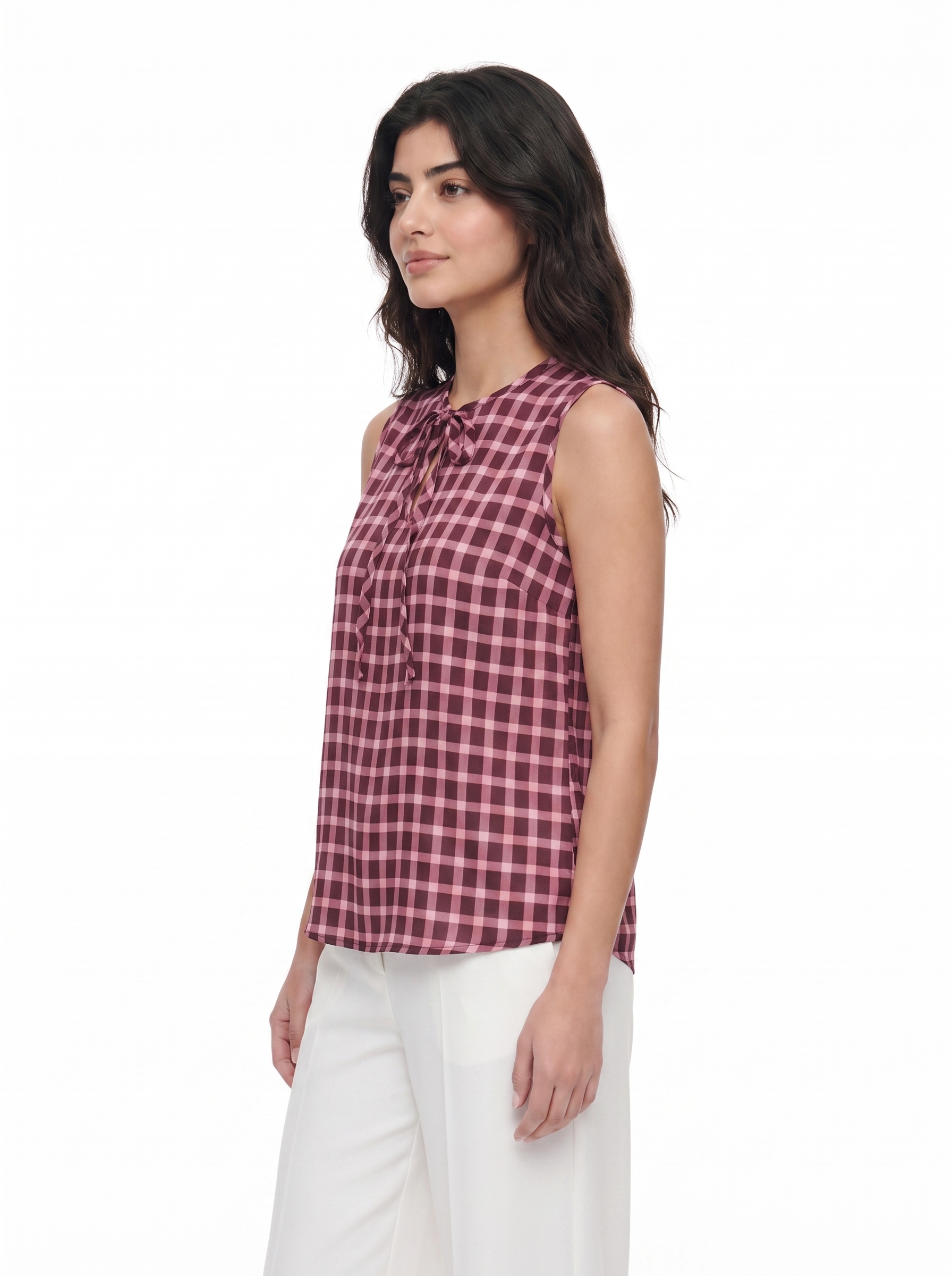 A woman wearing a sleeveless red and black gingham check top with a tie-neck detail, paired with white pants, photographed against a plain white background.