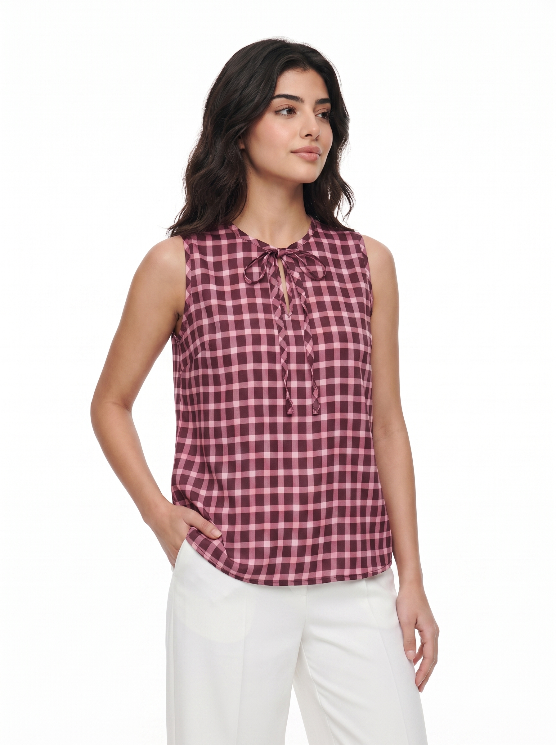 A woman modeling a sleeveless gingham top in a dusty rose and white check pattern with a tie-neck detail, paired with white pants, against a plain white background.