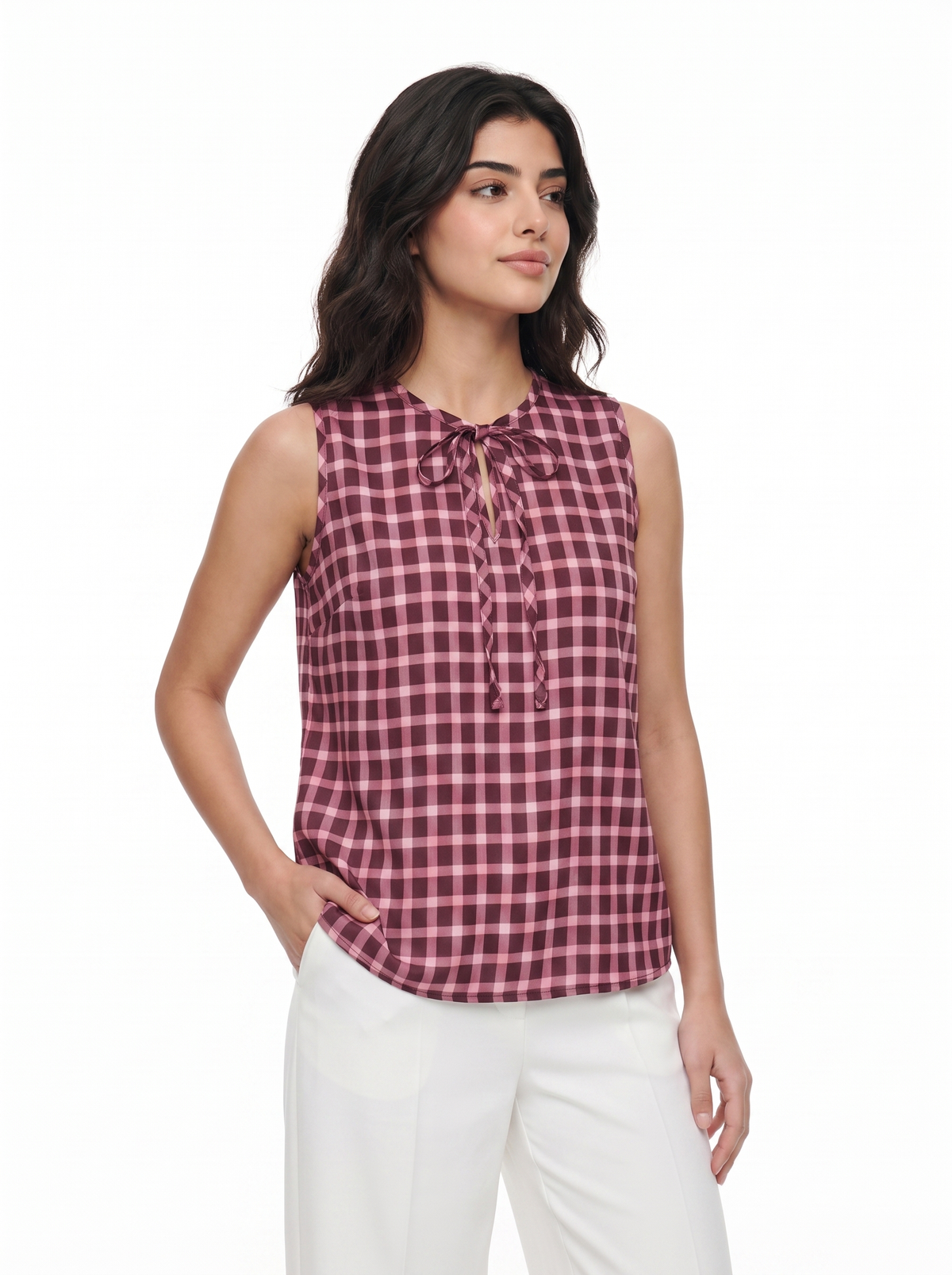 A woman modeling a sleeveless gingham top in a dusty rose and white check pattern with a tie-neck detail, paired with white pants, against a plain white background.