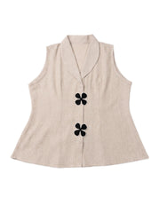 A sleeveless beige linen vest with a shawl collar and two black four-petal flower buttons, displayed flat against a white background.