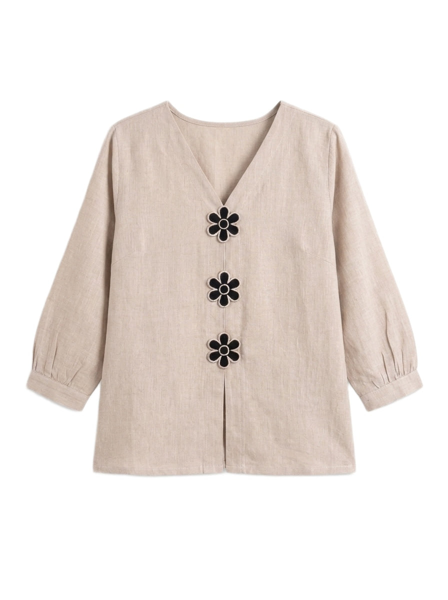 A beige linen long-sleeve blouse with a V-neckline and three black flower-shaped buttons down the front, displayed on a clean white background.