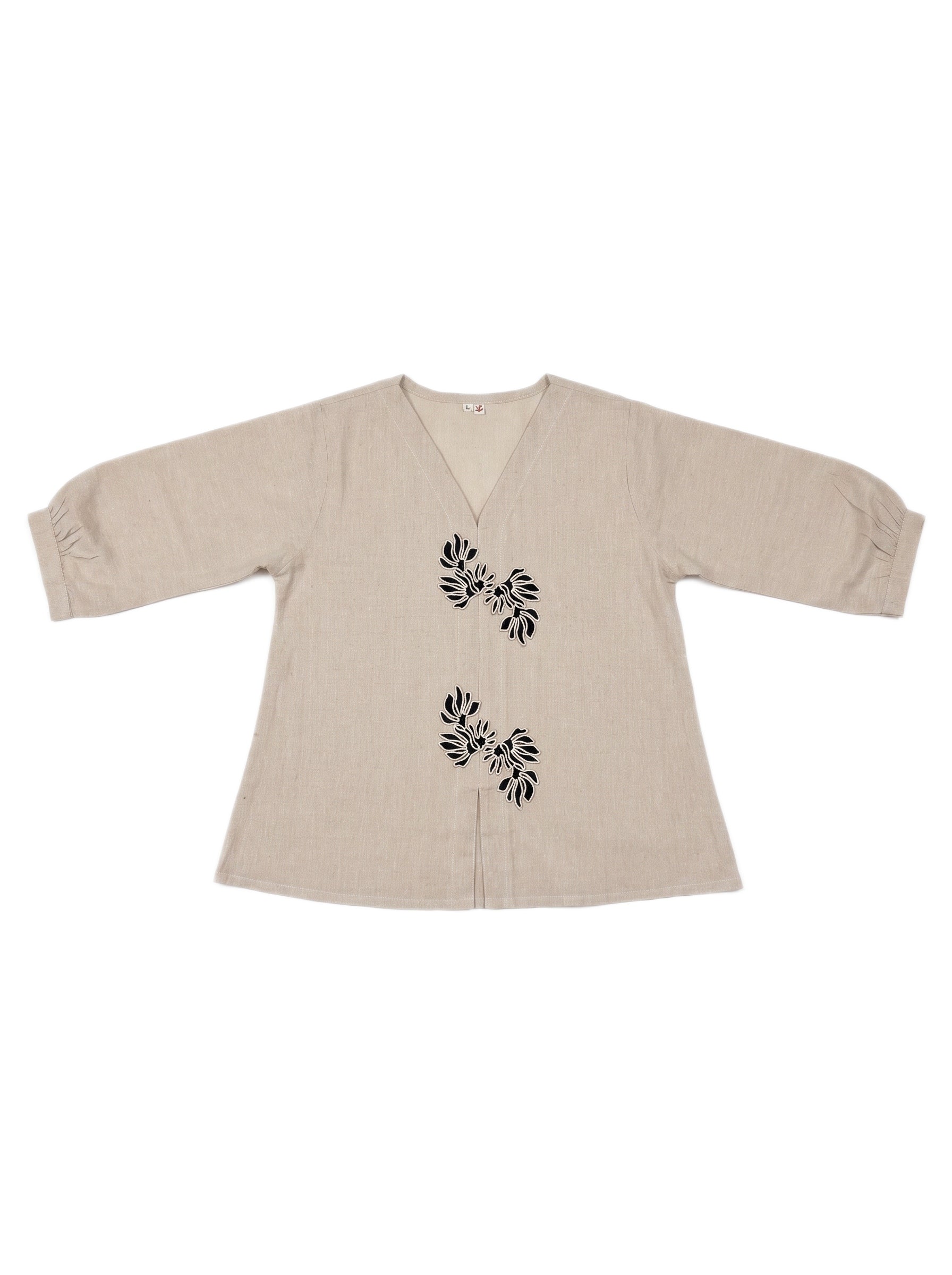 A beige linen long-sleeve top with black leaf embroidery on the front, displayed flat against a white background.