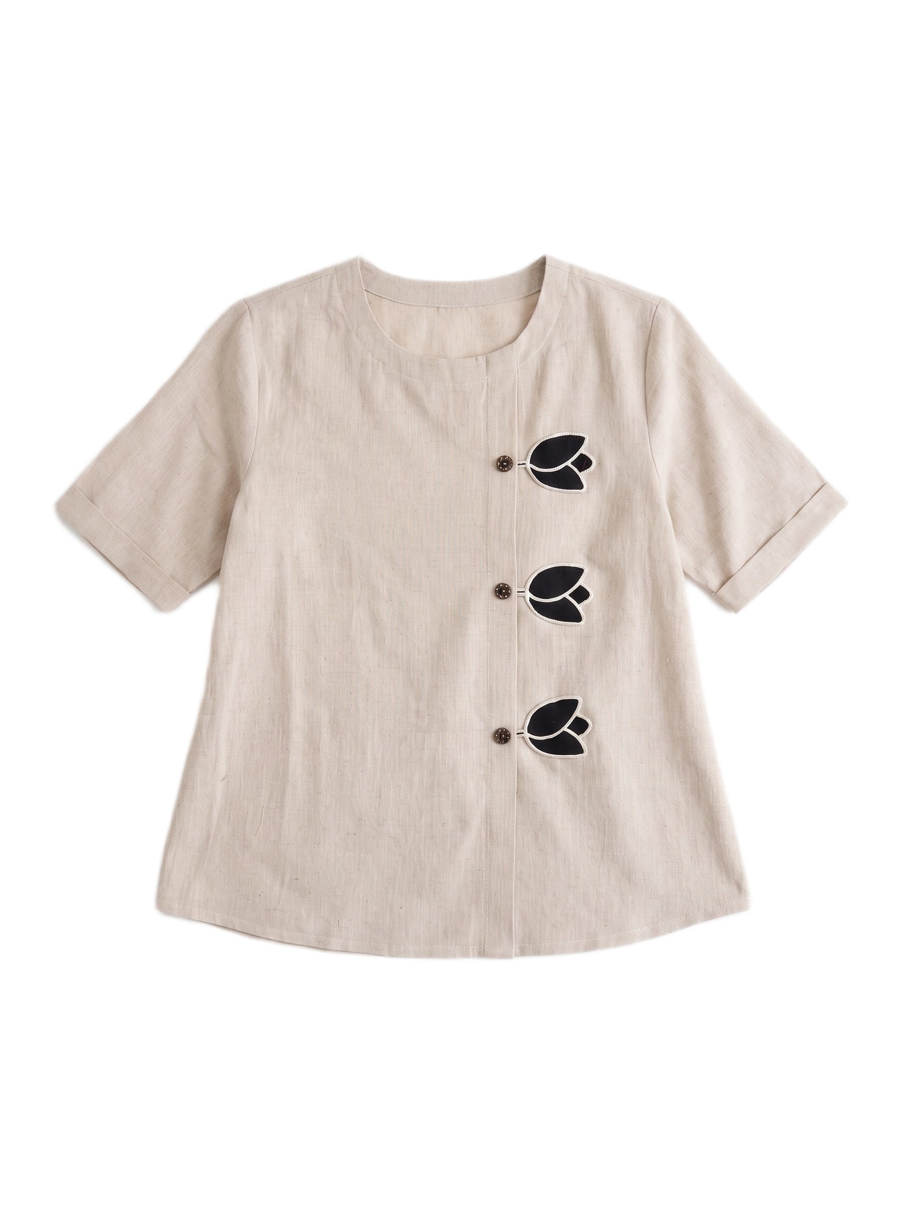 A beige short-sleeve linen top with three black embroidered leaf motifs and matching buttons down the front, displayed on a clean white background.