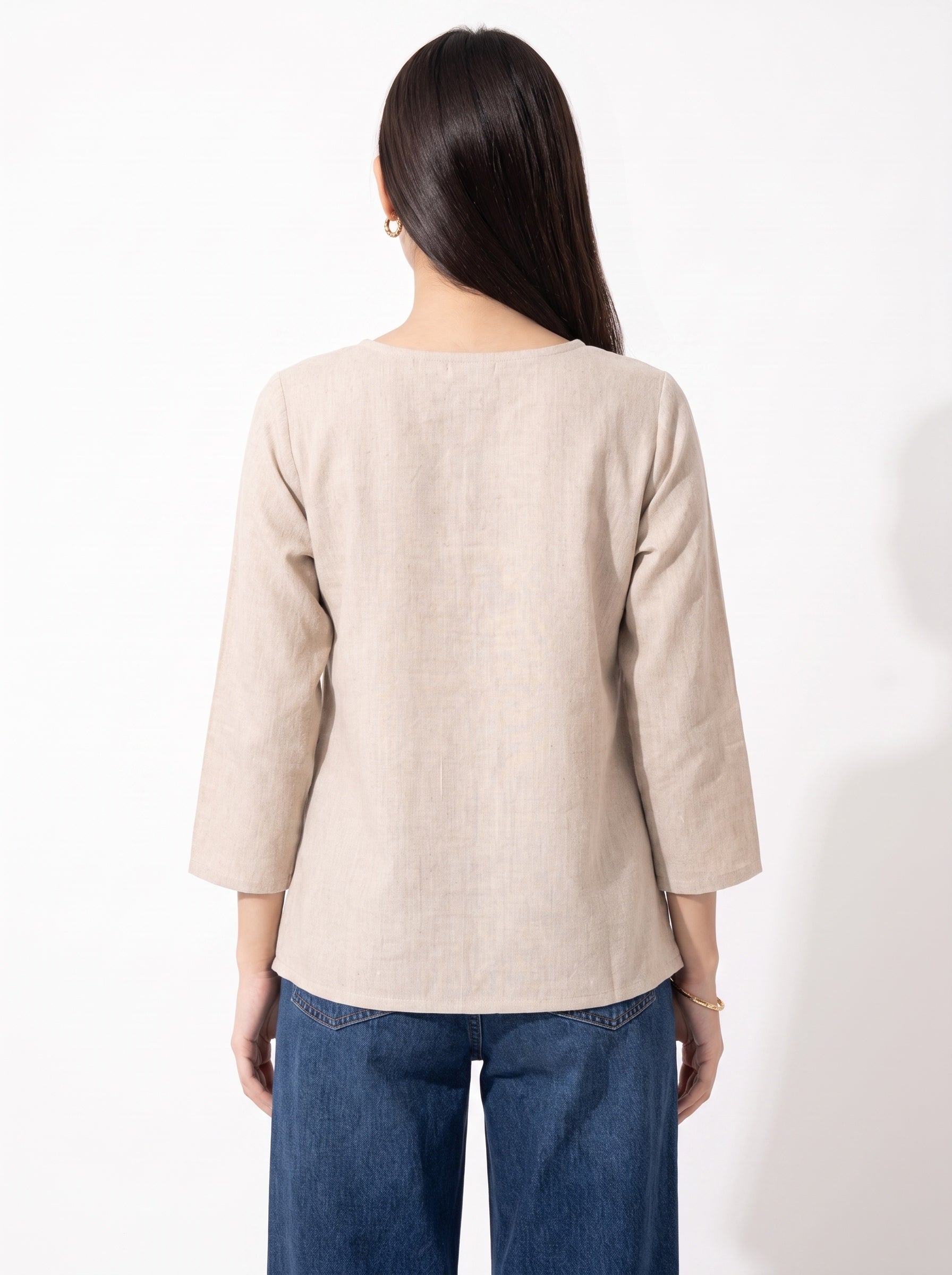 A woman viewed from the back wearing a light beige linen three-quarter sleeve top and blue jeans against a plain white background.