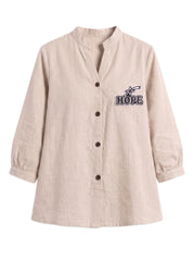 A light beige linen long-sleeve button-up shirt with a stand collar and a black embroidered graphic on the left chest that reads 'HOPE' with a star design, shown on a plain white background.