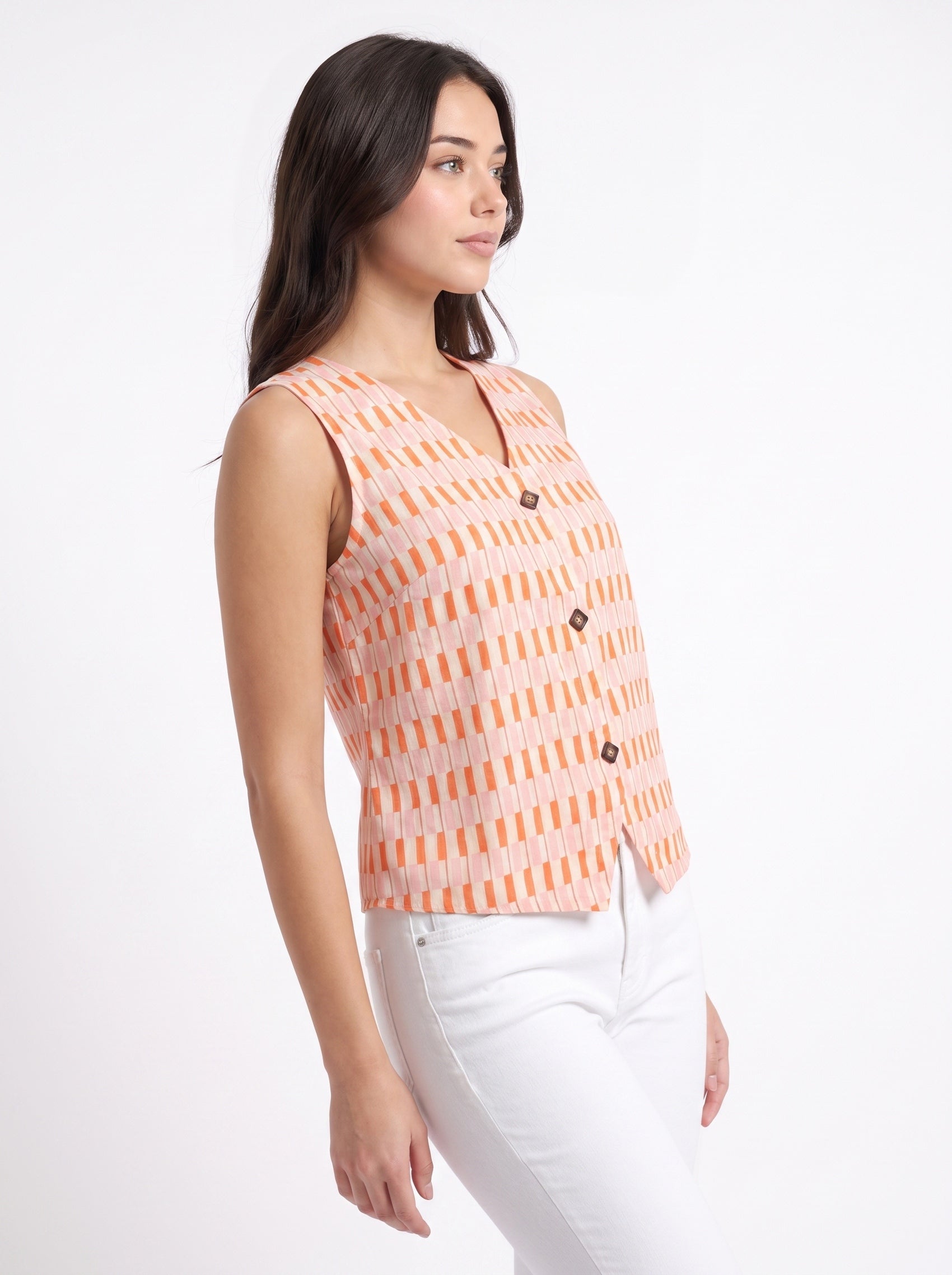 A woman wearing a sleeveless orange and white patterned vest with dark buttons, paired with white pants, photographed against a plain white studio background.