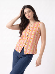 A woman modeling a sleeveless button-front vest with vertical peach and cream stripes and yellow polka dots, paired with dark blue jeans, against a plain white studio background.