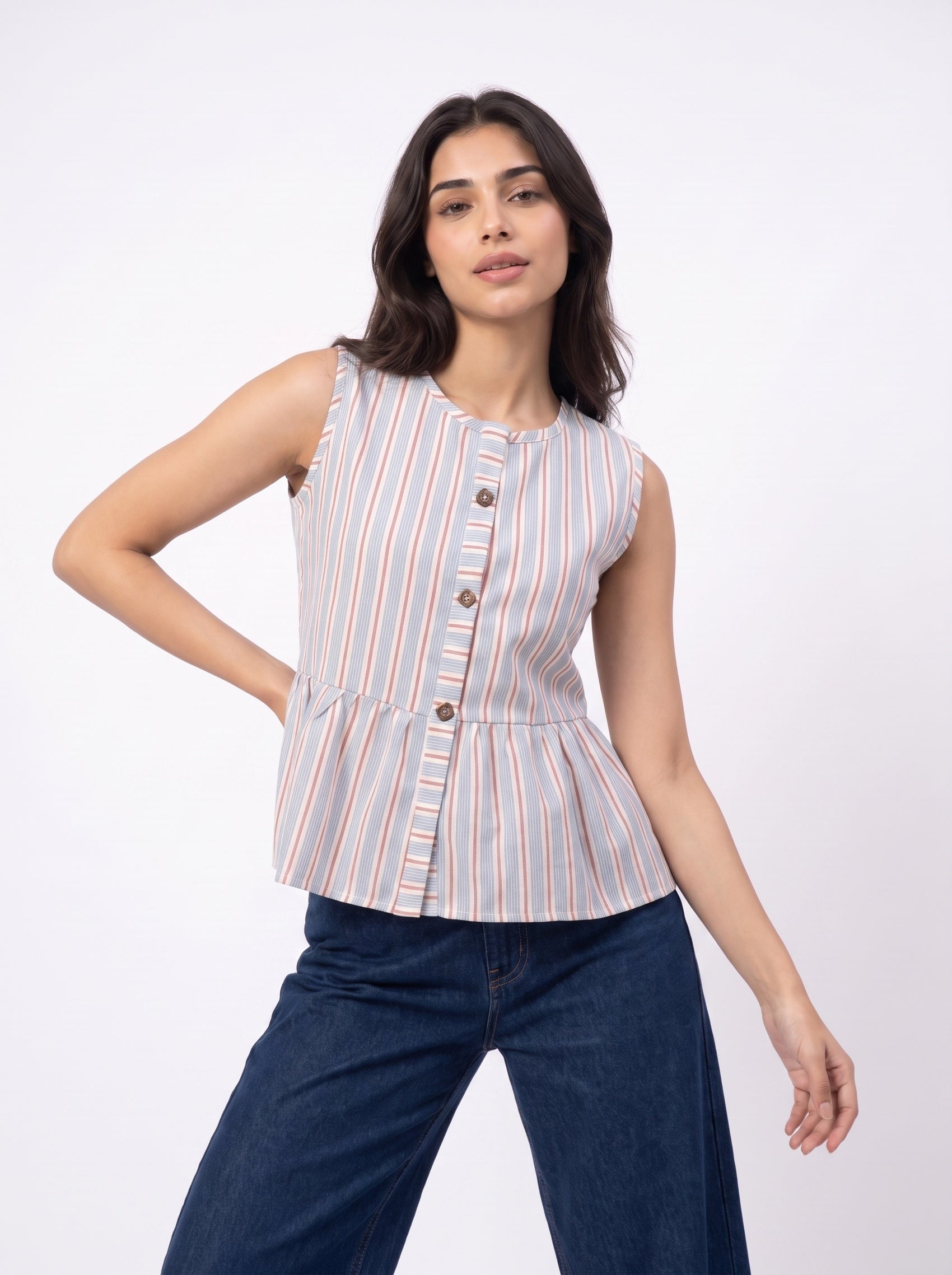 A woman modeling a sleeveless button-front peplum top with vertical stripes in beige, orange, and white, paired with dark blue jeans, against a plain white studio background.
