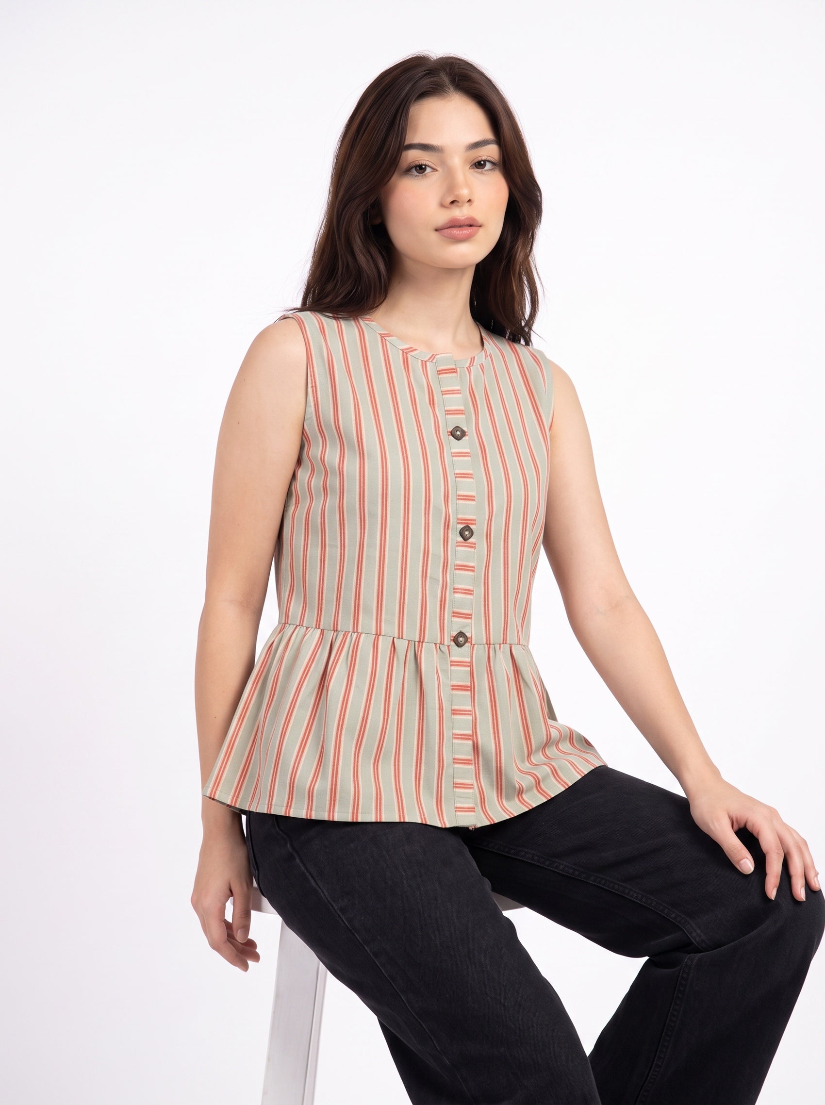 A woman wearing a sleeveless peplum top with vertical stripes in beige, orange, and white, paired with black pants, seated against a plain white background.