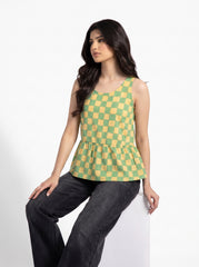 A woman wearing a sleeveless green and yellow checkered peplum top paired with dark gray jeans, posing against a clean white background.