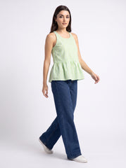 A woman modeling a sleeveless light green and white vertically striped peplum top paired with dark blue jeans and white sneakers, set against a plain light gray studio background.