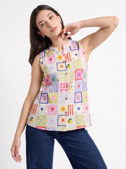 A woman modeling a sleeveless button-up blouse with a colorful patchwork print of squares and small motifs, paired with dark blue jeans, against a plain white studio background.