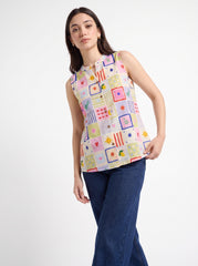 A woman modeling a sleeveless button-up top with a colorful patchwork print of geometric shapes and stars on a light pink base, paired with dark blue jeans, against a plain white studio background.