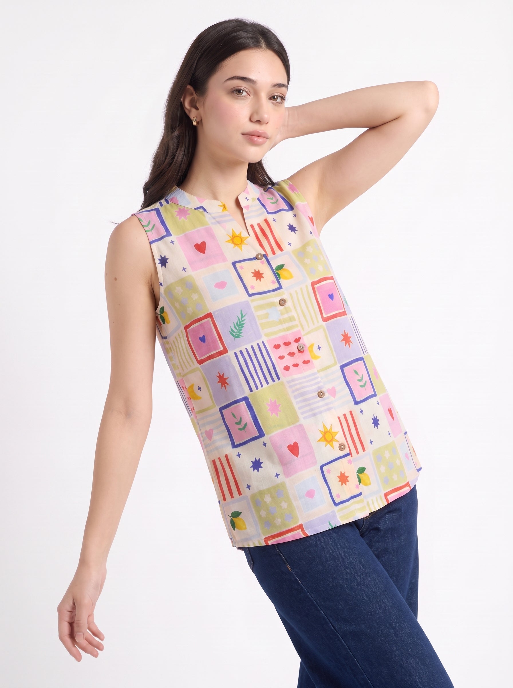 A woman modeling a sleeveless collared top with a colorful patchwork print, paired with dark blue jeans, against a plain white studio background.
