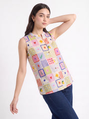 A woman modeling a sleeveless collared top with a colorful patchwork print, paired with dark blue jeans, against a plain white studio background.
