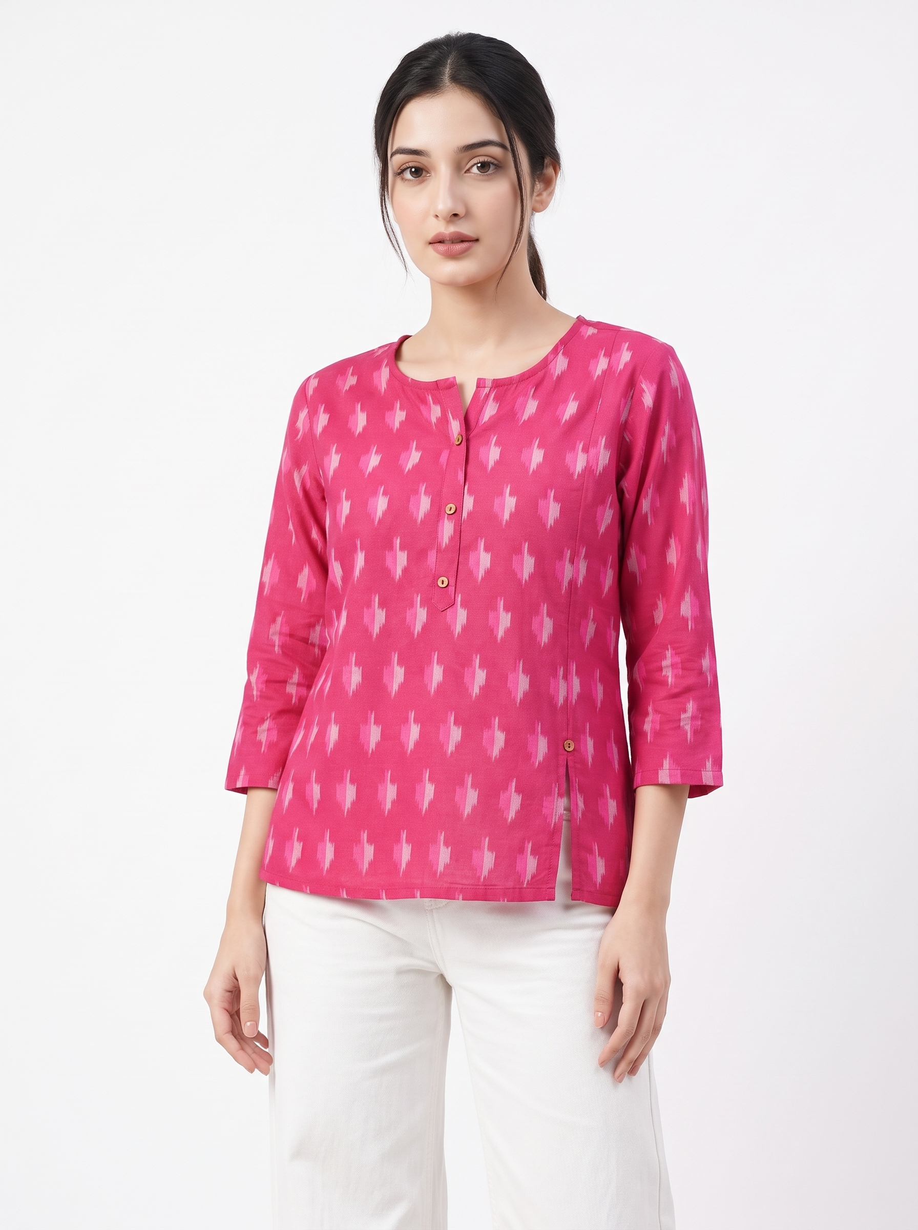 A woman modeling a bright pink three-quarter sleeve top with a white ikat pattern, paired with white pants, against a plain white studio background.