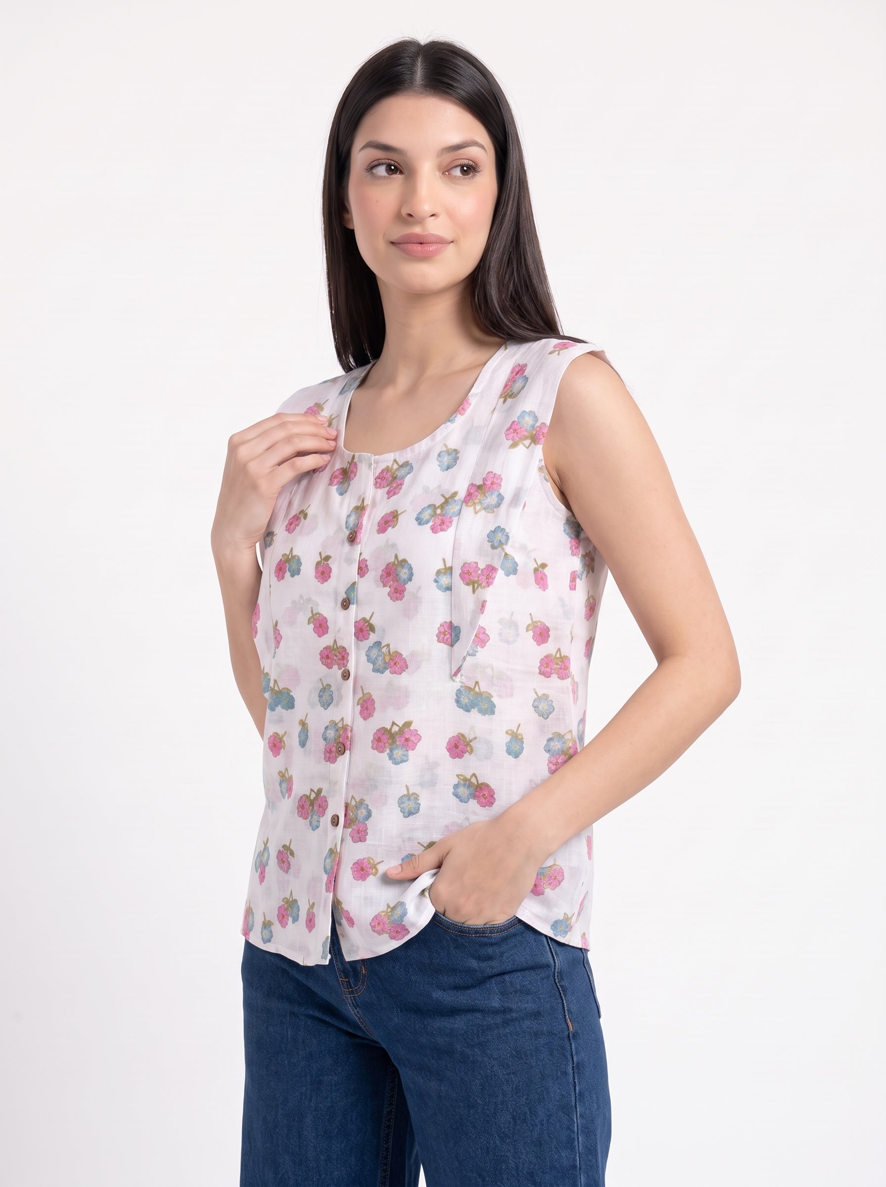 A woman modeling a sleeveless white top with a pink and blue floral pattern, paired with dark blue jeans, against a plain white background.