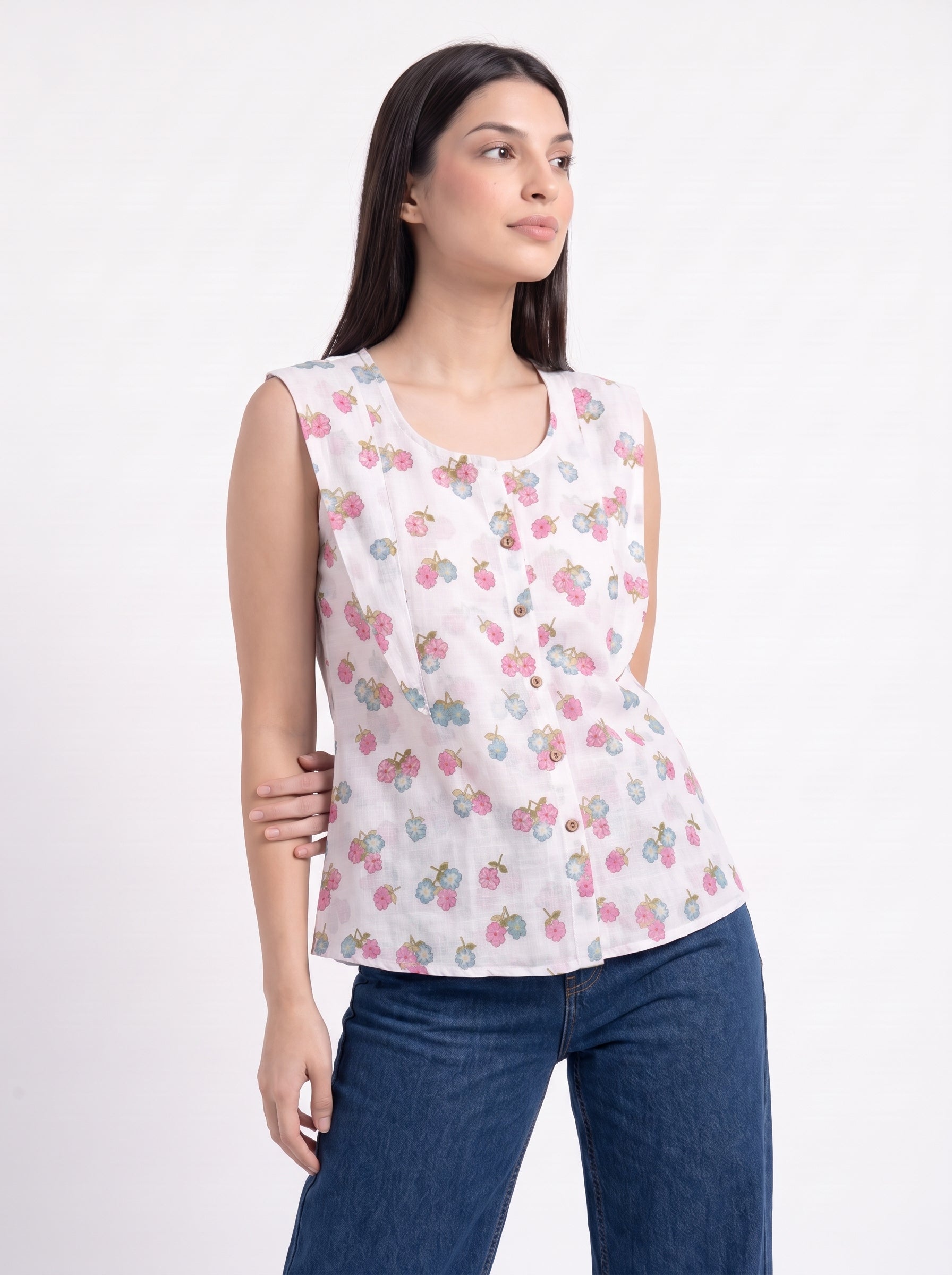 A woman modeling a sleeveless white top with a pink and green strawberry print, paired with blue jeans, against a plain white background.