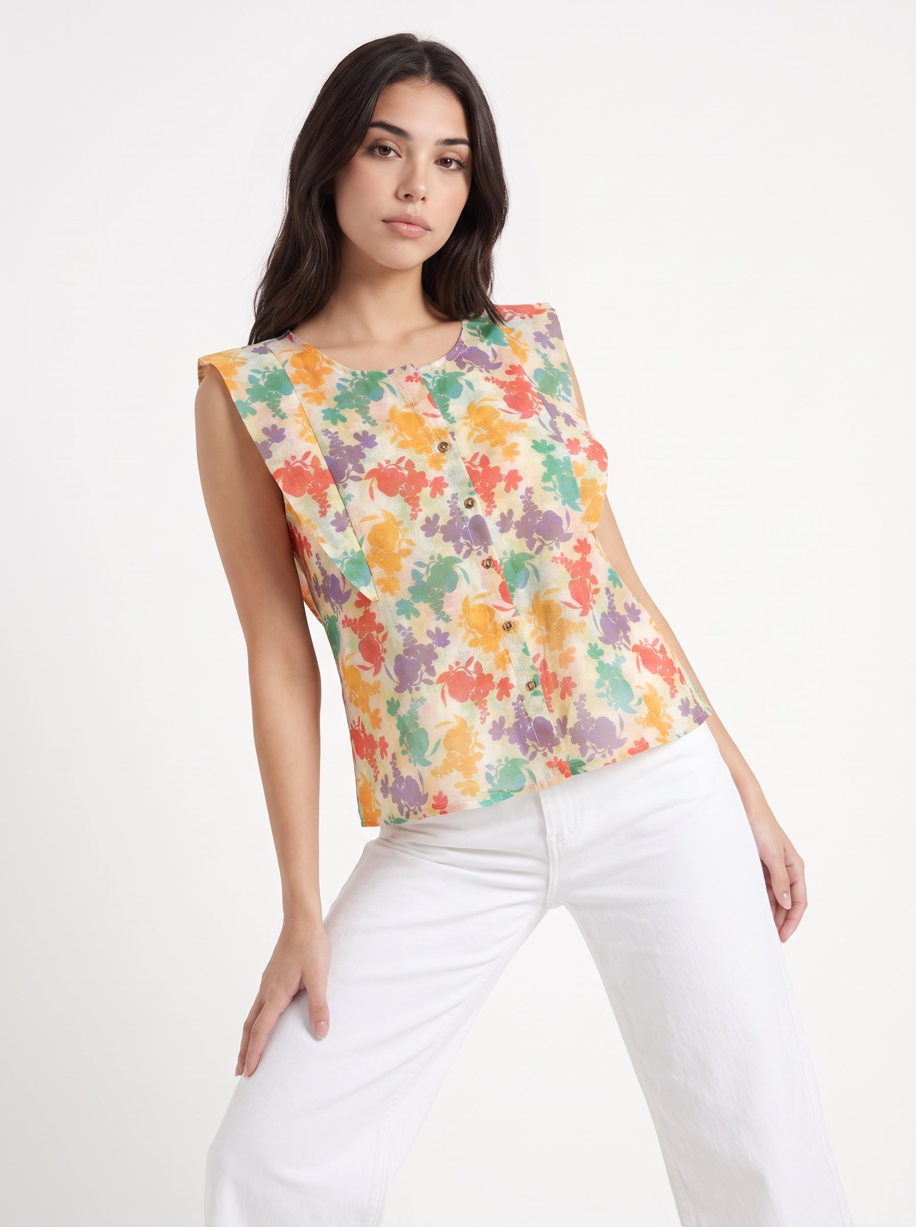 A woman modeling a sleeveless button-front top with a colorful abstract floral print on a cream background, paired with white pants, against a plain white studio background.