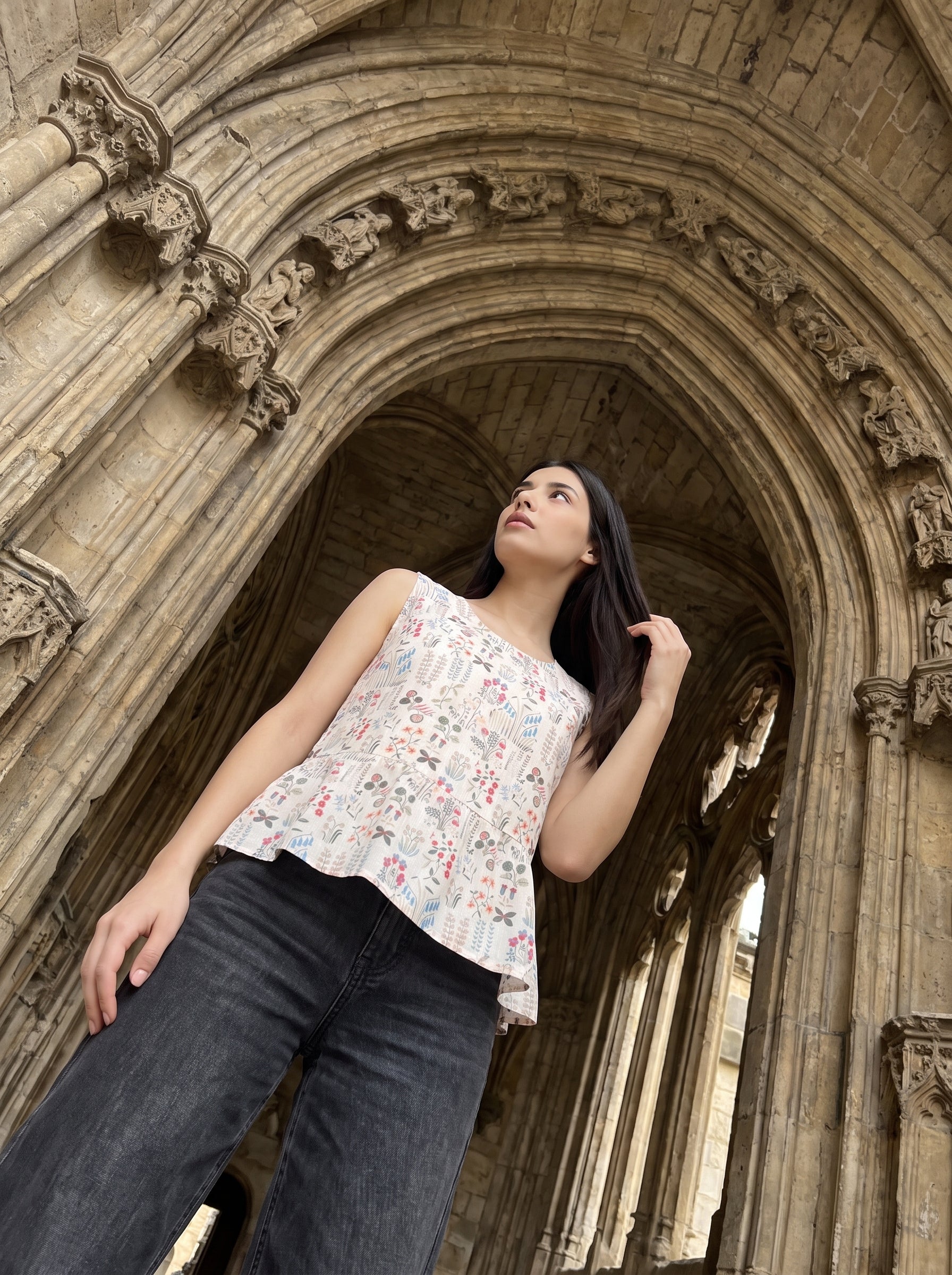 A graceful beige sleeveless top featuring delicate multicolor botanical motifs in soft red, blue, green, and earthy tones
