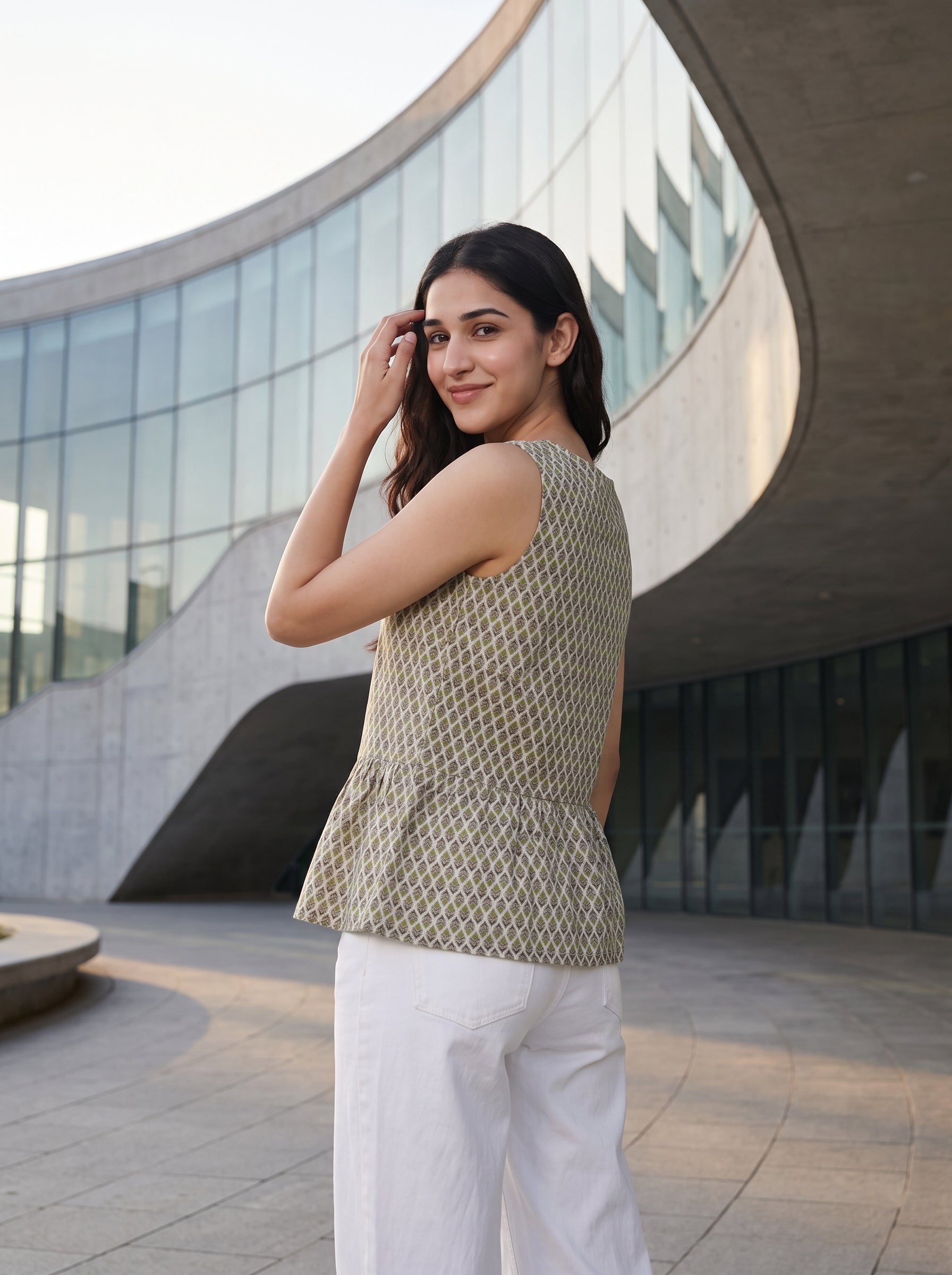 A woman in a patterned beige top and white pants stands in a gallery, looking at a large colorful pop-art style painting on the wall.