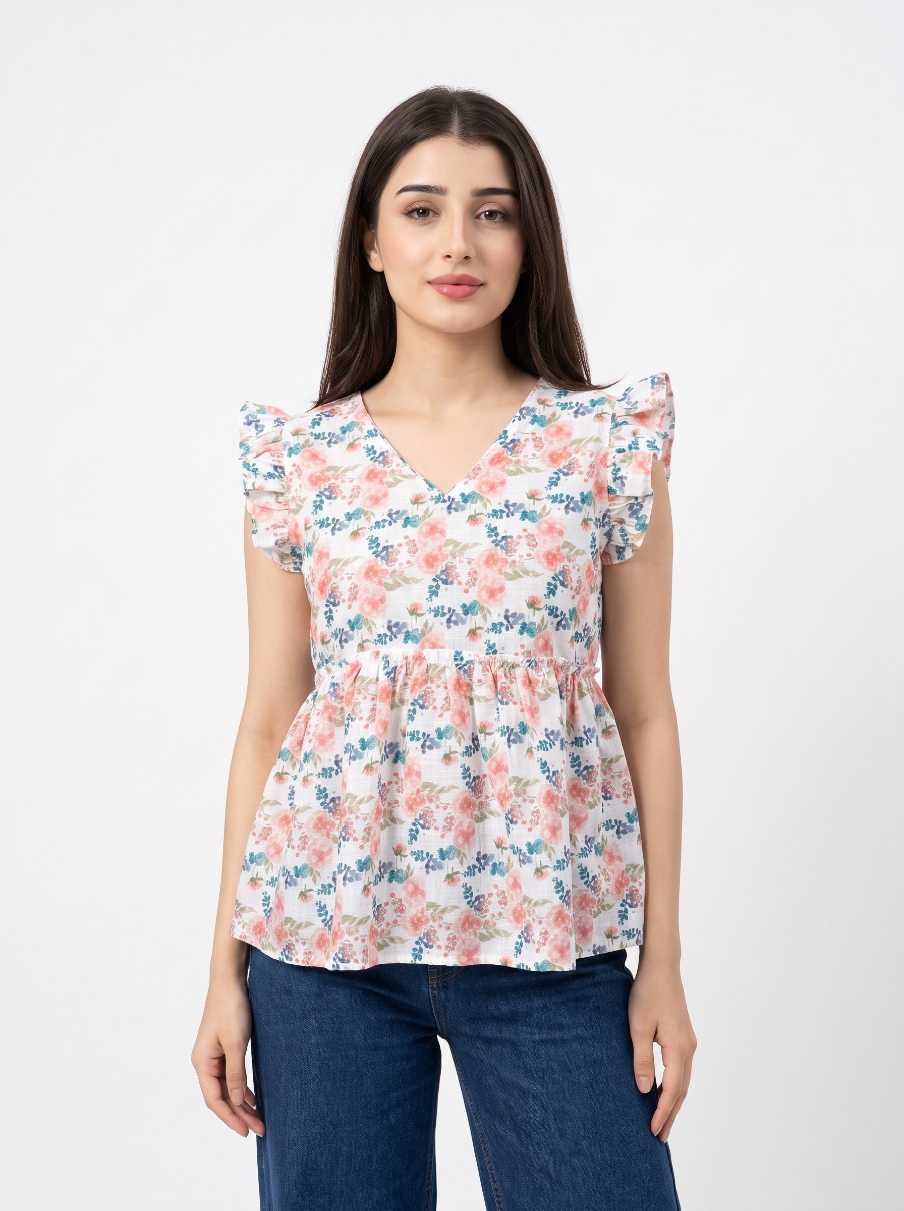 A woman modeling a short-sleeve peplum blouse with a pink, blue, and green floral pattern on a white background, paired with dark blue jeans, against a plain light gray studio background.