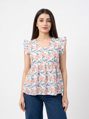 A woman modeling a short-sleeve peplum blouse with a pink, blue, and green floral pattern on a white background, paired with dark blue jeans, against a plain light gray studio background.