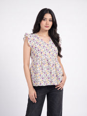 A woman modeling a sleeveless V-neck blouse with a purple and yellow floral print on a white base, paired with dark gray jeans, against a plain white studio background.