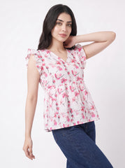 A woman modeling a white short-sleeve blouse with a pink floral print and ruffled shoulders, paired with dark blue jeans, against a plain white studio background.