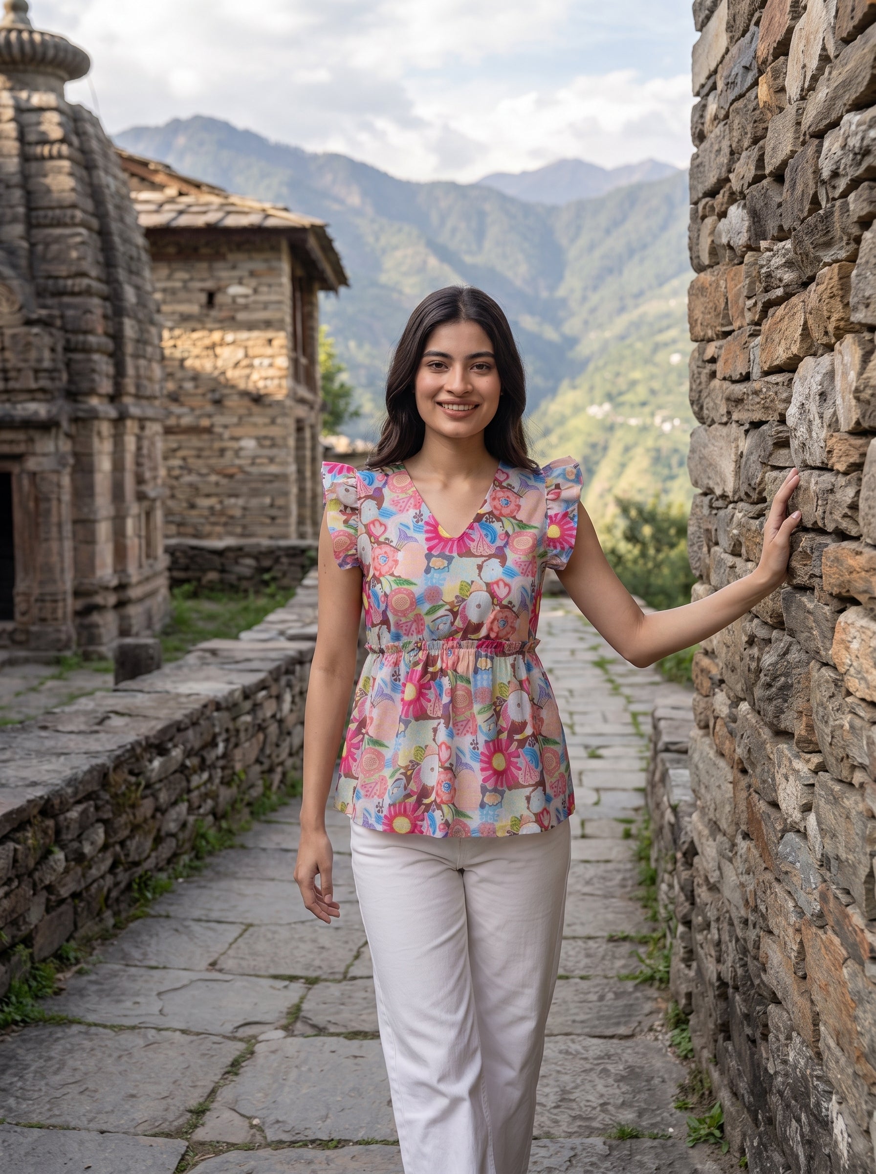 A lively off-white top featuring bright pink, blue, green, peach, and yellow floral motifs for a cheerful statement look. The V-neckline and layered ruffle sleeves add a playful feminine touch, while the gathered peplum waist creates a flattering, flowy silhouette.