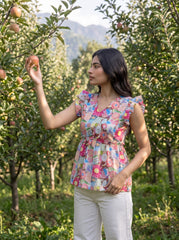 A lively off-white top featuring bright pink, blue, green, peach, and yellow floral motifs for a cheerful statement look. The V-neckline and layered ruffle sleeves add a playful feminine touch, while the gathered peplum waist creates a flattering, flowy silhouette.