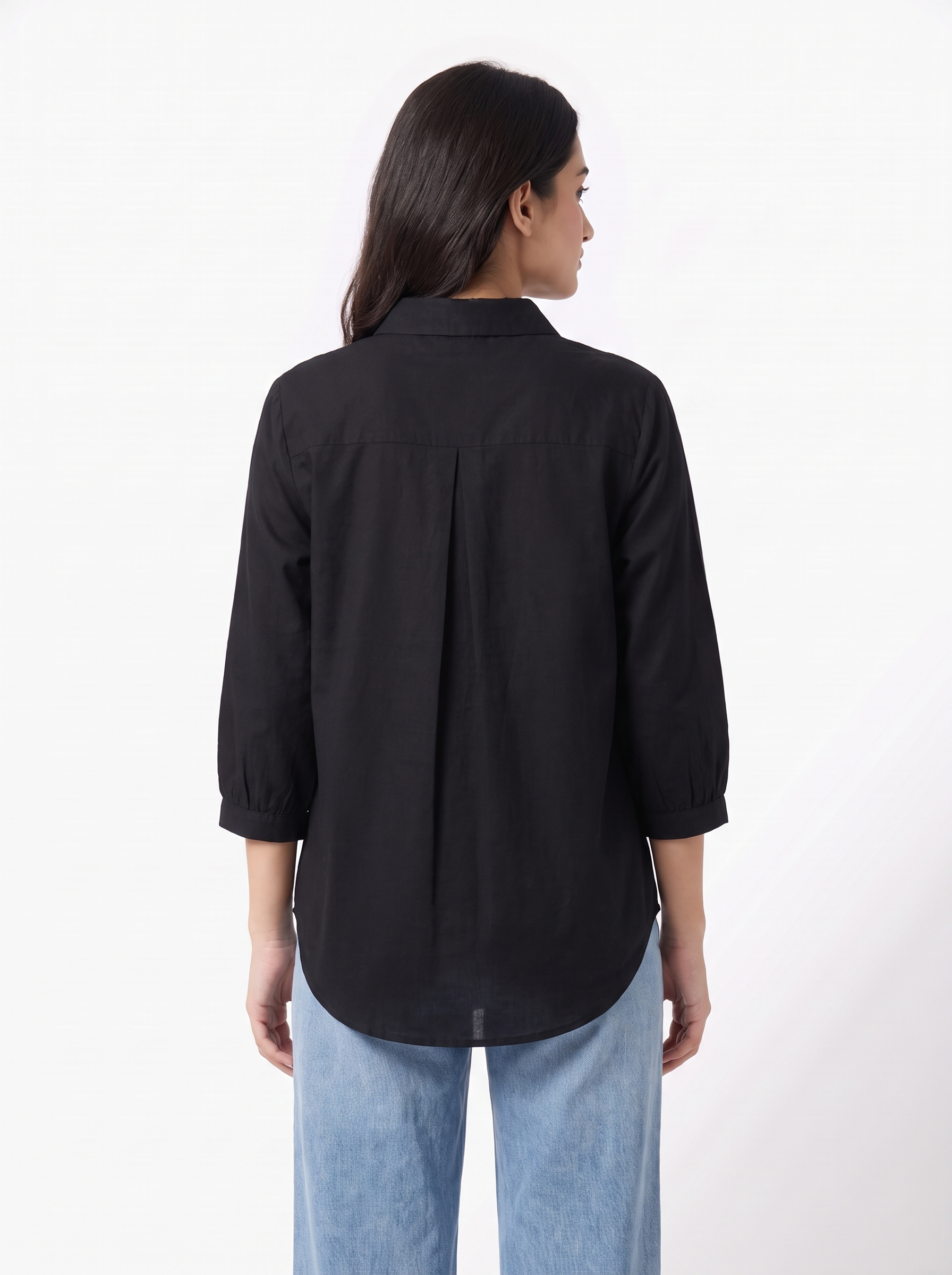 A woman shown from the back wearing a black long-sleeve button-up shirt with a subtle pleat detail at the back hem, paired with light blue jeans, against a plain white studio background.