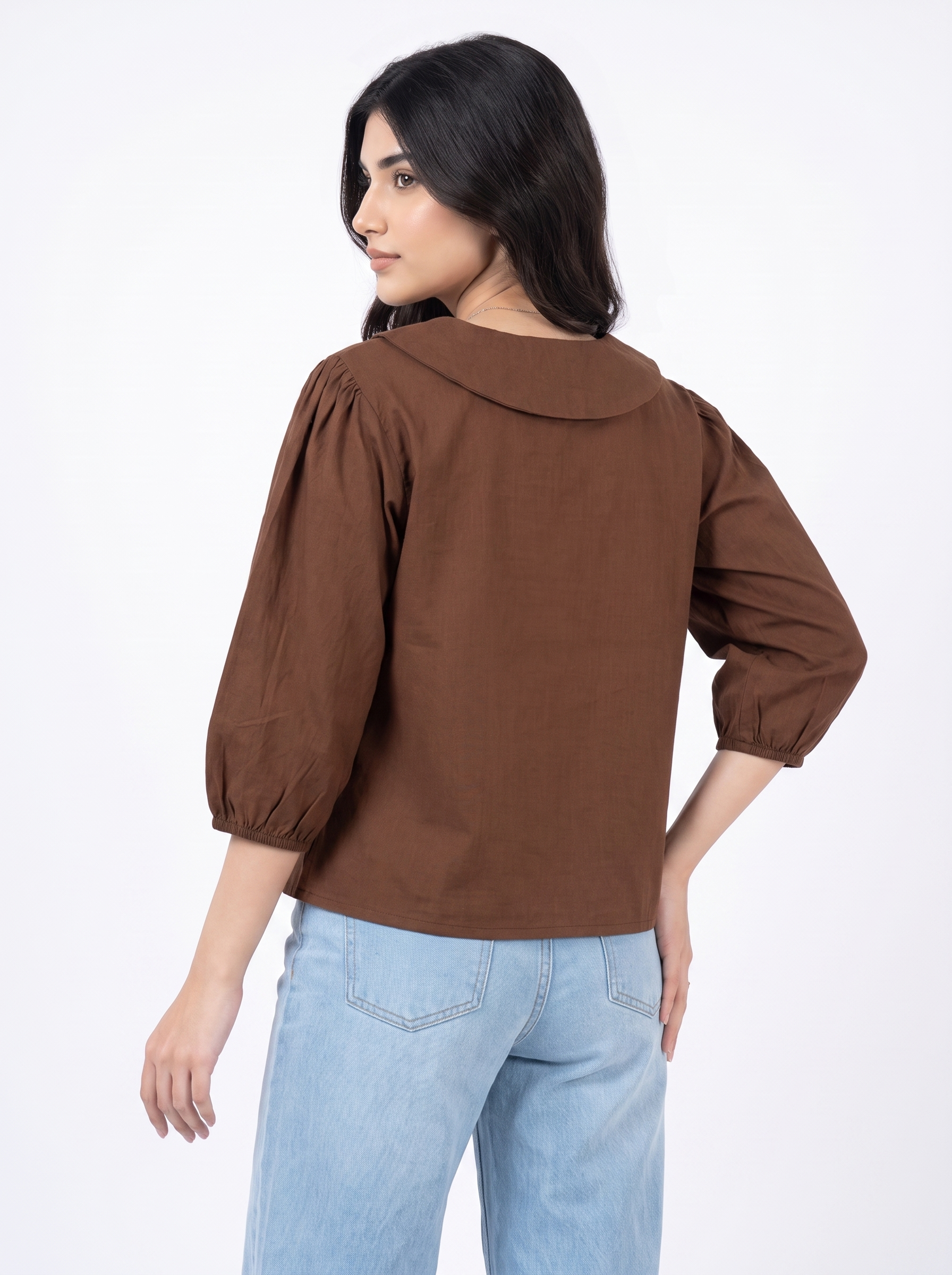 A woman wearing a brown long-sleeve blouse with puff sleeves and a round collar, shown from the back against a plain white studio background.