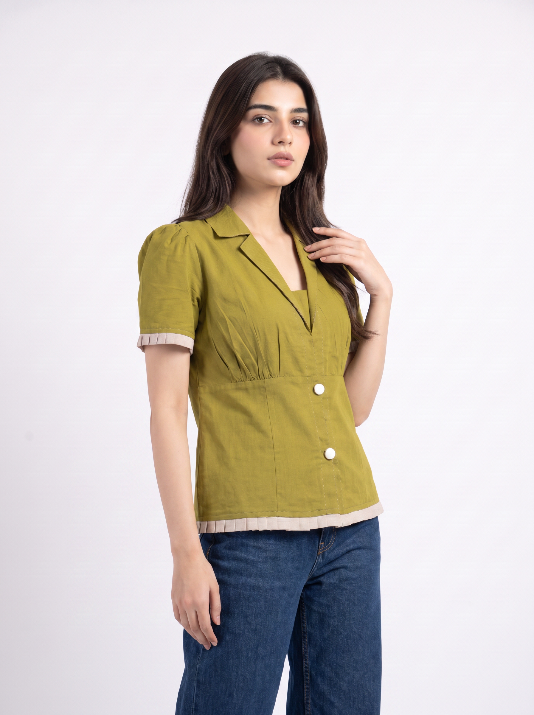 A woman modeling a short-sleeve olive green top with beige trim and white buttons, paired with blue jeans, against a plain white studio background.