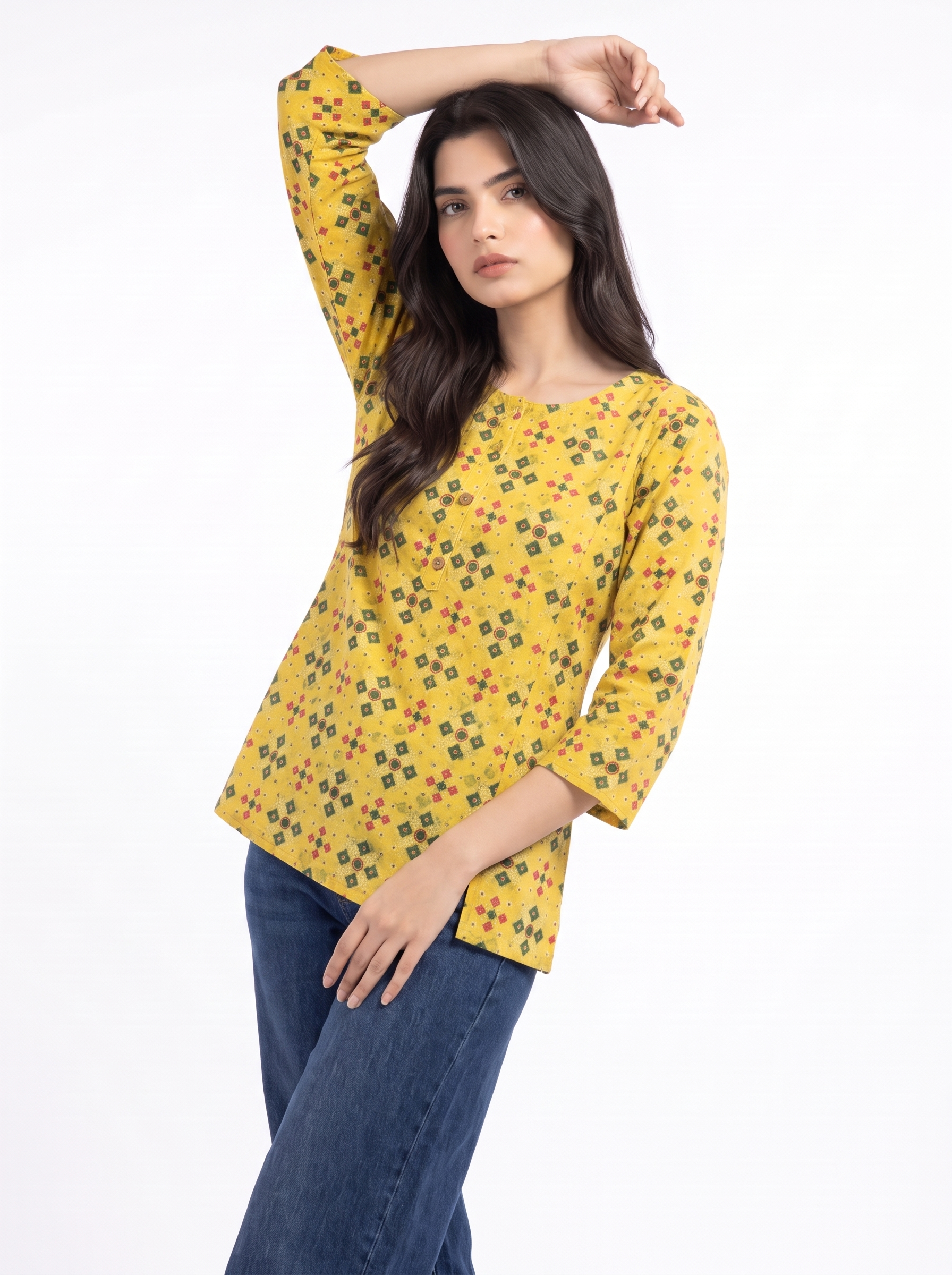 A woman modeling a yellow three-quarter sleeve top with a small geometric multicolor print, paired with blue jeans, against a plain white background.